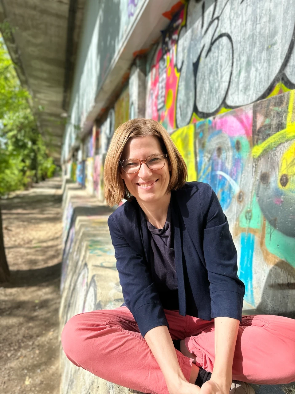 Ulrike Gartler sitzt auf einer Bank vor einer bemalten Wand am Grazer Murufer - Berufliche Neurorientierung